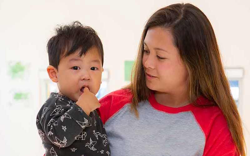 Young toddler feeling sad, being held by teacher